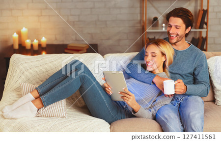 Happy Millennial Couple Using Tablet Computer Watching Movie Relaxing On Couch At Home. Cozy Evening Together Happy Millennial Couple Using Tablet Computer Watching Movie Relaxing On Couch At Home. Cozy Evening Together 127411561