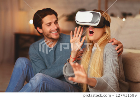 Excited Spouses Using VR Headset Experiencing Virtual Reality And Having Fun Sitting Indoor. Modern Home Entertainment. 127411599