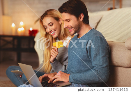 Online Order. Boyfriend And Girlfried Holding Laptop And Credit Card Shopping On The Internet Sitting Indoor. Selective Focus 127411613