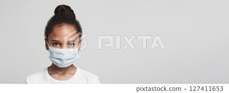 Infection concept. Portrait of little african american girl wearing medical mask, grey background 127411653