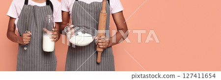 Cropped image of african sisters holding kitchen tools, flour and milk, kids and cooking concept, red background, cropped 127411654