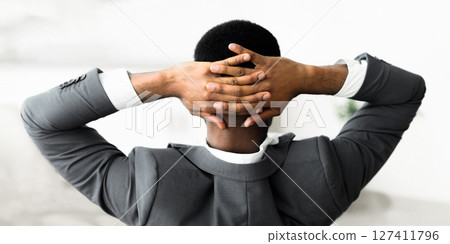 A man in a suit leans back with his arms crossed behind his head. A man in a suit leans back with his arms crossed behind his head. 127411796