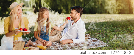 Family Having Picnic In Park After Quarantine, Daughter Feeding Father With Apple Enjoying Summer Day Together. Panorama 127411860