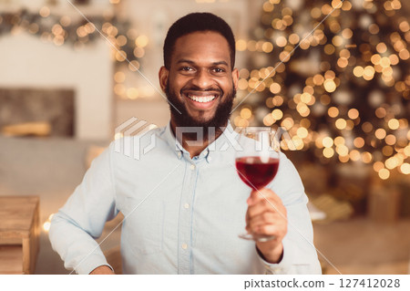 Celebration Concept. Portrait of smiling handsome young bearded african american man holding glass of red wine, toasting and looking to camera, blurred background, selective focus Celebration Concept. Portrait of smiling handsome young bearded african american man holding glass of red wine, toasting and looking to camera, blurred background, selective focus 127412028