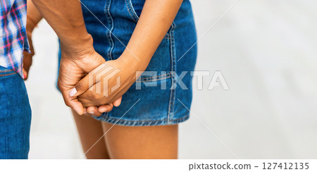 A close-up shot of a couple holding hands, both wearing denim clothing. Guy is wearing a plaid shirt and jeans, while the girl is wearing a denim skirt. Their hands are clasped together, copy space 127412135