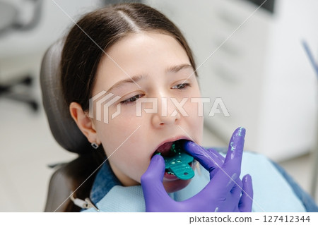 Dentist placing impression tray in girl's mouth for dental care 127412344