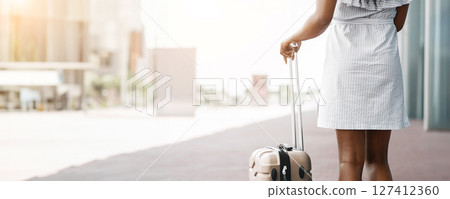 Cropped of woman walking away from the camera with a piece of luggage. She is wearing a light-colored dress and appears to be in an urban setting, copy space Cropped of woman walking away from the camera with a piece of luggage. She is wearing a light-colored dress and appears to be in an urban setting, copy space 127412360