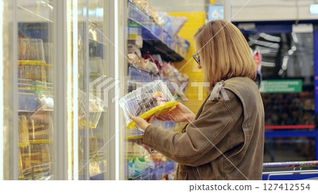 Customer making purchasing decisions for refrigerated packaged desserts in grocery store based on product quality and variety Customer making purchasing decisions for refrigerated packaged desserts in grocery store based on product quality and variety 127412554