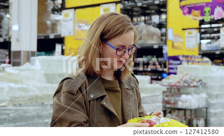 Young woman carefully selecting fresh tomatoes from a bag in the produce section of a modern supermarket, focusing on quality and ripeness 127412580