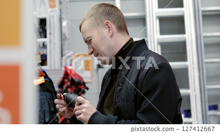 Man carefully examines power tool packaging to ensure it fits his requirements while browsing in a hardware store. A man in a hardware store choosing a tool. 127412667