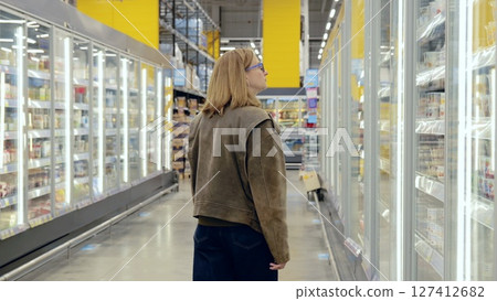 Young woman browsing refrigerated dairy products in a grocery store, walking through the aisles of chilled shelves 127412682