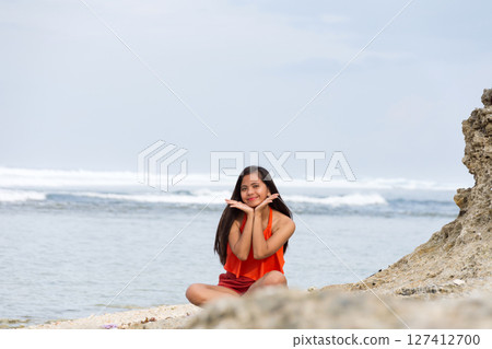 Happy woman sitting on the beach with waves in the background Happy woman sitting on the beach with waves in the background 127412700