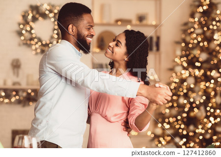 Couple In Love. Smiling young african american man and woman dancing at home. Happy black family of two enjoying time together, celebrating event, holiday, anniversary or St Valentine's day 127412860