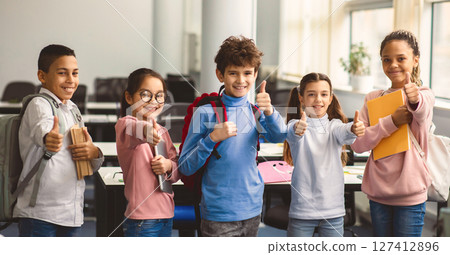 Education Concept. Diverse group of happy smiling international classmates standing in line with notebooks and backpacks in classroom and showing thumbs up sign gesture, enjoying studying at school Education Concept. Diverse group of happy smiling international classmates standing in line with notebooks and backpacks in classroom and showing thumbs up sign gesture, enjoying studying at school 127412896