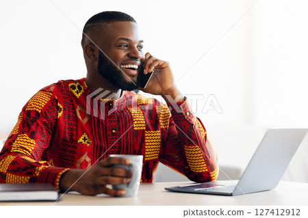 Handsome African Freelancer Guy Talking On Cellphone And Drinking Coffee, Resting At Desk In Home Office, Having Pleasant Phone Conversation, Enjoying Working Remotely And Online Job, Copy Space Handsome African Freelancer Guy Talking On Cellphone And Drinking Coffee, Resting At Desk In Home Office, Having Pleasant Phone Conversation, Enjoying Working Remotely And Online Job, Copy Space 127412912