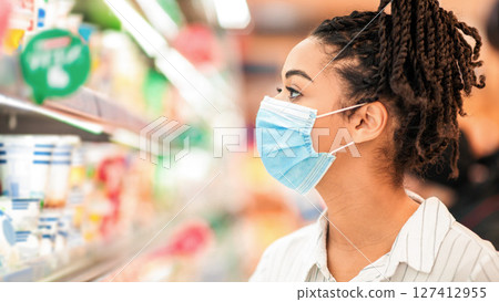 African Lady Wearing Face Mask Shopping Food Products And Groceries In Supermarket, Standing Near Shelves In Shop Aisle Choosing Goods In Groceries Store Indoors. Female Customer Buyer Portrait 127412955