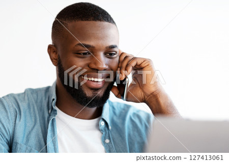Closeup Portrait Of Smiling Black Man Talking On Cellphone And Using Laptop In Office. Handsome African American Entrepreneur Enjoying Phone Conversation While Working On Computer, Selective Focus 127413061