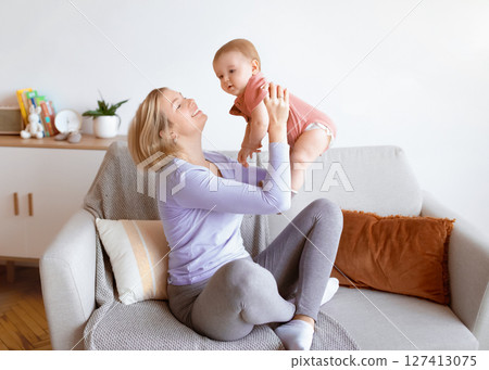 Loving blonde mother bonding with her little cute kid at home, living room interior, copy space. Happy young woman lifting up her baby boy or girl, enjoying time together. Motherhood concept Loving blonde mother bonding with her little cute kid at home, living room interior, copy space. Happy young woman lifting up her baby boy or girl, enjoying time together. Motherhood concept 127413075