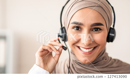 Closeup portrait of cheerful female doctor muslim woman with headset talking to patient, copy space. Smiling young lady in hijab having conversation with patient, touching microphone Closeup portrait of cheerful female doctor muslim woman with headset talking to patient, copy space. Smiling young lady in hijab having conversation with patient, touching microphone 127413090