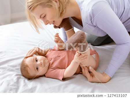 Mother and kid concept. Loving caucasian mother cuddling with her beautiful little baby at home, laying together on bed. Blonde woman looking at her cute kid toddler, closeup 127413107