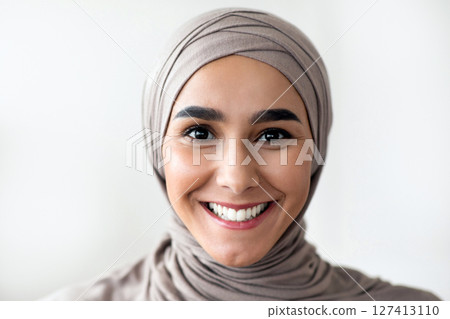 Portrait of cheerful young woman in hijab doctor or patient over clinic interior, copy space. Muslim lady in beautiful headscarf physician smiling at camera, working at clinic, closeup 127413110