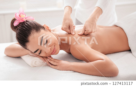 Beautiful young asian woman relaxing during back massage session in spa salon, enjoying recovery body treatment from professional masseur, lying on table with closed eyes and smiling, closeup Beautiful young asian woman relaxing during back massage session in spa salon, enjoying recovery body treatment from professional masseur, lying on table with closed eyes and smiling, closeup 127413117