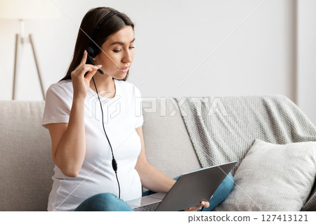 Young Pregnant Woman With Headset And Laptop At Home Study Or Working Remotely, Millennial Expectant Woman Sitting At Couch With Computer, Learning Online Or Having Distance Job, Free Space Young Pregnant Woman With Headset And Laptop At Home Study Or Working Remotely, Millennial Expectant Woman Sitting At Couch With Computer, Learning Online Or Having Distance Job, Free Space 127413121