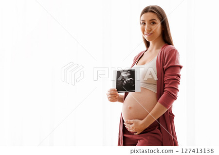 Cute Pregnant Lady Posing With Baby Sonography Photo Near Window At Home, Beautiful Expectant Lady Tenderly Touching Her Belly And Smiling At Camera, Enjoying Healthy Pregnancy And Future Maternity Cute Pregnant Lady Posing With Baby Sonography Photo Near Window At Home, Beautiful Expectant Lady Tenderly Touching Her Belly And Smiling At Camera, Enjoying Healthy Pregnancy And Future Maternity 127413138