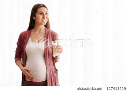 Happy Pregnant Lady Enjoying Healthy Calcium Drink, Holding Glass With Milk While Standing Near Window At Home, Young Smiling Expectant Lady Tenderly Embracing Belly And Looking Away, Copy Space Happy Pregnant Lady Enjoying Healthy Calcium Drink, Holding Glass With Milk While Standing Near Window At Home, Young Smiling Expectant Lady Tenderly Embracing Belly And Looking Away, Copy Space 127413219