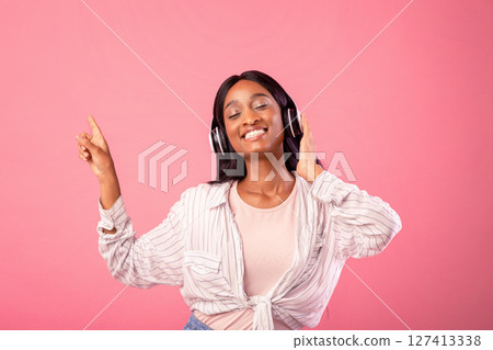 Gorgeous black lady with headset listening to music and dancing with closed eyes, pointing aside on pink studio background. Pretty African American woman moving to her favorite melody Gorgeous black lady with headset listening to music and dancing with closed eyes, pointing aside on pink studio background. Pretty African American woman moving to her favorite melody 127413338
