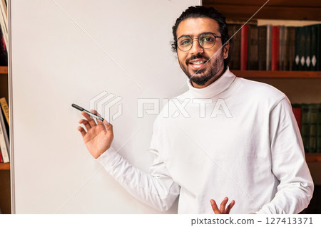 Knowledge And Education. Indian Male Teacher Teaching Online Pointing To Blackboard With English Language Grammar Rules Standing Indoor, Smiling To Camera. Distance Teaching And Learning Concept Knowledge And Education. Indian Male Teacher Teaching Online Pointing To Blackboard With English Language Grammar Rules Standing Indoor, Smiling To Camera. Distance Teaching And Learning Concept 127413371