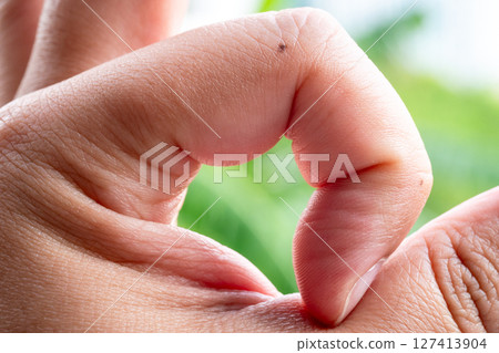 Hand gesture creating heart shape nature background close-up peaceful environment emotional connection 127413904