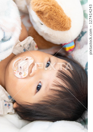 One year old asian girl with pacifier and toy cozy indoor setting close-up 127414243