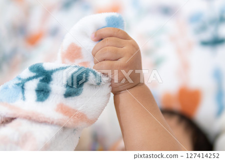 One year old asian girl grasping soft blanket cozy room close-up perspective childhood joy 127414252