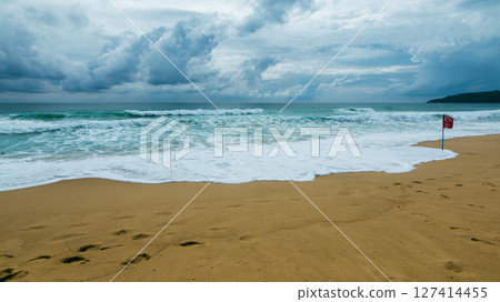 Waves crashing sandy beach with warning flag coastal area nature landscape dramatic clouds 127414455