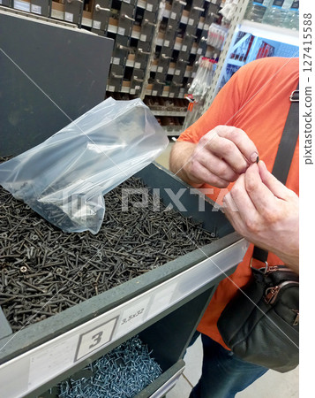 A man examines screws in a hardware store, carefully selecting the right ones from a bulk bin 127415588