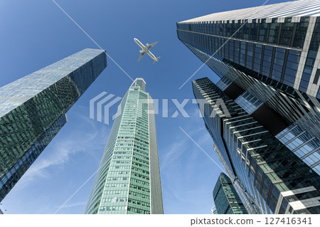 Modern glass skyscrapers on a clear day and passenger aircraft flying over them Modern glass skyscrapers on a clear day and passenger aircraft flying over them 127416341