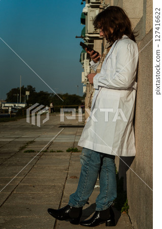 Young female doctor using phone while leaning on hospital wall 127416622