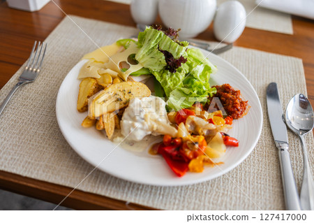 Plate with salad, roasted vegetables, potatoes, and cheese on dining table. Healthy lunch option, balanced nutrition, and hotel meal concept. Plate with salad, roasted vegetables, potatoes, and cheese on dining table. Healthy lunch option, balanced nutrition, and hotel meal concept. 127417000