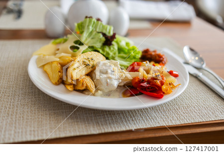 Plate with salad, roasted vegetables, potatoes, and cheese on dining table. Healthy lunch option, balanced nutrition, and hotel meal concept. Plate with salad, roasted vegetables, potatoes, and cheese on dining table. Healthy lunch option, balanced nutrition, and hotel meal concept. 127417001