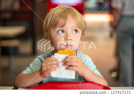 Young child enjoying fast food meal in a casual dining environment. Four year old boy happily eating in a restaurant. Kids diet, bad food choices, early junk food addiction Young child enjoying fast food meal in a casual dining environment. Four year old boy happily eating in a restaurant. Kids diet, bad food choices, early junk food addiction 127417171