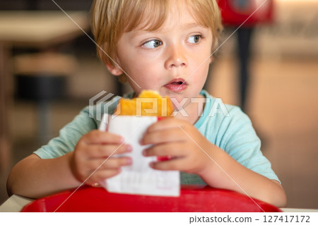 Young child enjoying fast food meal in a casual dining environment. Four year old boy happily eating in a restaurant. Kids diet, bad food choices, early junk food addiction 127417172