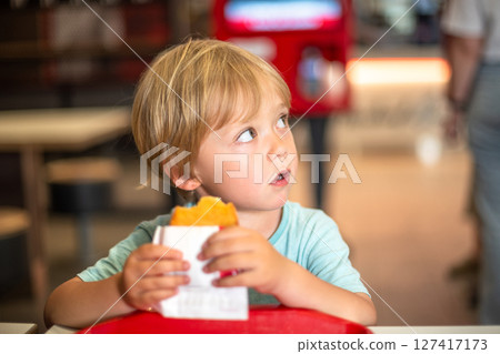 Young child enjoying fast food meal in a casual dining environment. Four year old boy happily eating in a restaurant. Kids diet, bad food choices, early junk food addiction 127417173