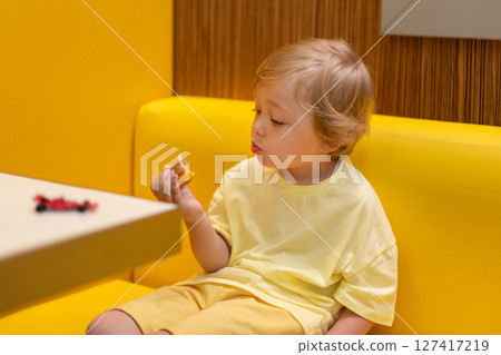 A small child wearing a yellow shirt is eating chicken nuggets in a vibrant environment. Four year old boy enjoying fast food meal. Kids diet, bad food choices, early junk food addiction 127417219
