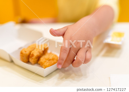 A small child wearing a yellow shirt is eating chicken nuggets in a vibrant environment. Four year old boy enjoying fast food meal. Kids diet, bad food choices, early junk food addiction 127417227