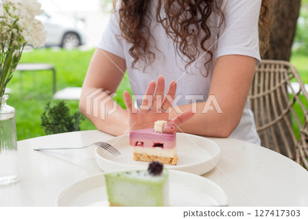 Woman Gesturing Near Colorful Cakes on White Plates in Outdoor Setting. No to sugar, diet concept, fasting, dieting, losing weight. No cakes, woman on a diet. 127417303