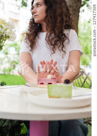 Woman Gesturing Near Colorful Cakes on White Plates in Outdoor Setting. No to sugar, diet concept, fasting, dieting, losing weight. No cakes, woman on a diet. Woman Gesturing Near Colorful Cakes on White Plates in Outdoor Setting. No to sugar, diet concept, fasting, dieting, losing weight. No cakes, woman on a diet. 127417309