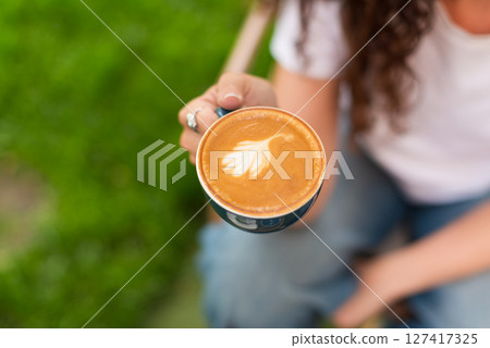 Woman enjoying a cup of coffee outdoors in a peaceful garden setting 127417325