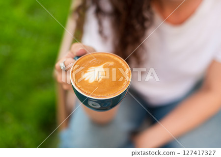 Woman enjoying a cup of coffee outdoors in a peaceful garden setting 127417327