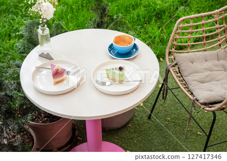 A cozy outdoor caf? table featuring two colorful desserts, a cup of coffee, and a vase of flowers, set against a vibrant garden background, offering a delightful and relaxing atmosphere. A cozy outdoor caf? table featuring two colorful desserts, a cup of coffee, and a vase of flowers, set against a vibrant garden background, offering a delightful and relaxing atmosphere. 127417346